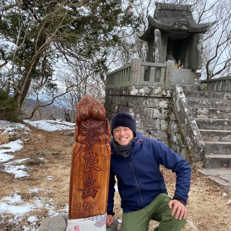 Issei at the summit of Mt. Tara (996 m), beside the summit marker and a stone shrine in winter